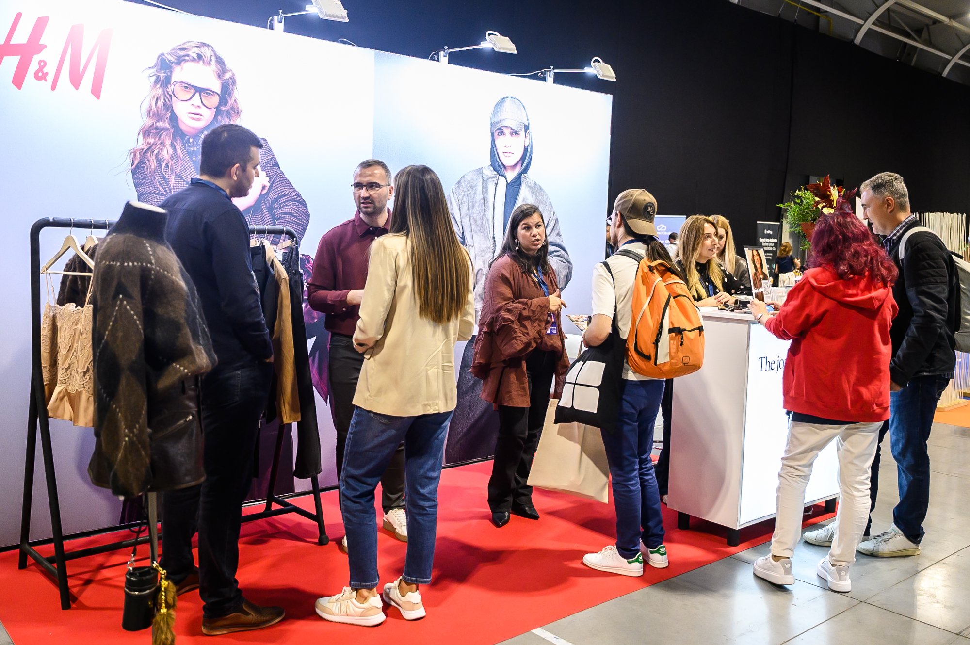 People gathered at an H&M booth with clothing racks and large fashion posters in a showroom.