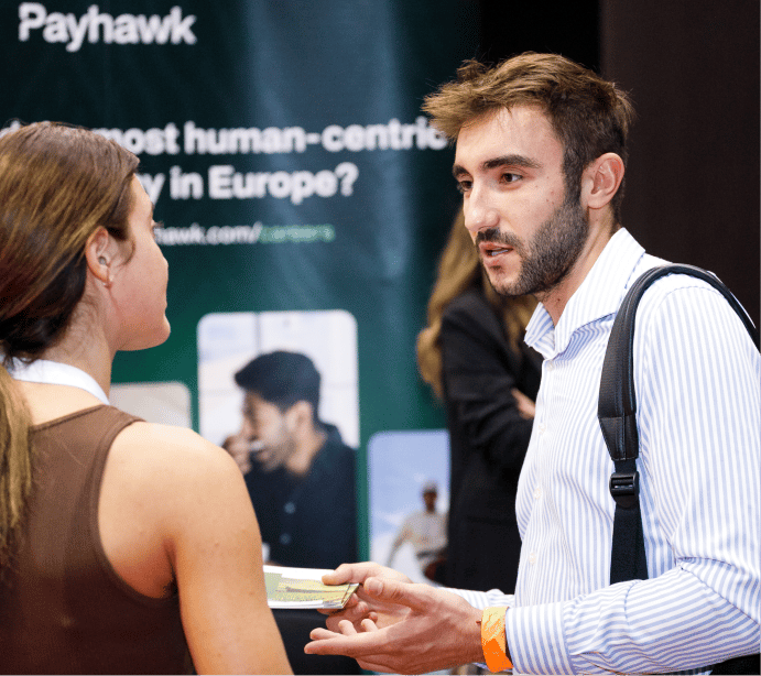 Medium shot photograph of two individuals talking, with a sign in background.